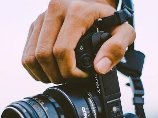 Close-up of a hand holding a vintage camera outdoors with a blurred green background, creating a bokeh effect.