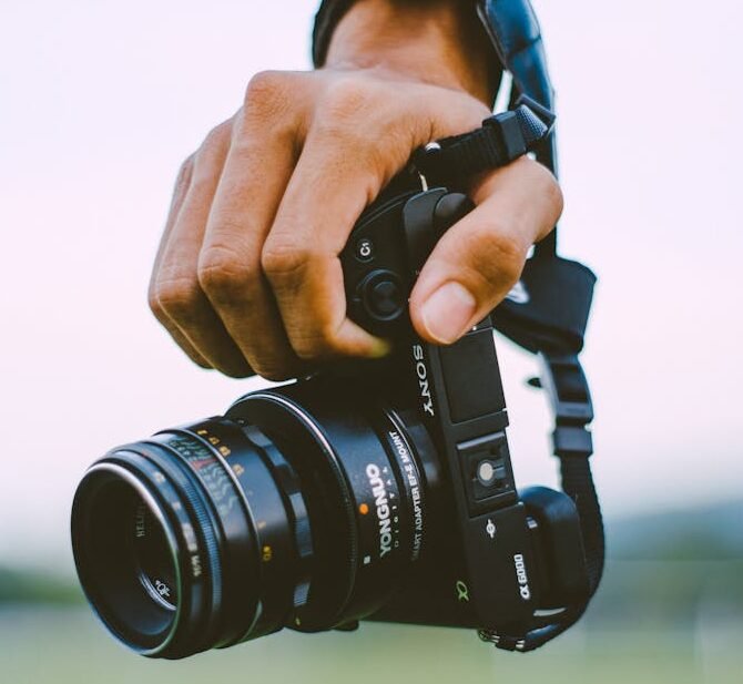 Close-up of a hand holding a vintage camera outdoors with a blurred green background, creating a bokeh effect.