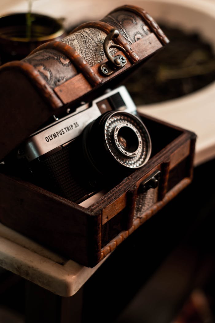 A vintage Olympus Trip 35 camera inside an antique wooden chest on a table.